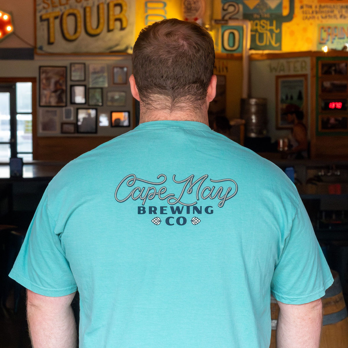Back view of a person in a turquoise Cape May Brewing Co. tee in the brewery tasting room