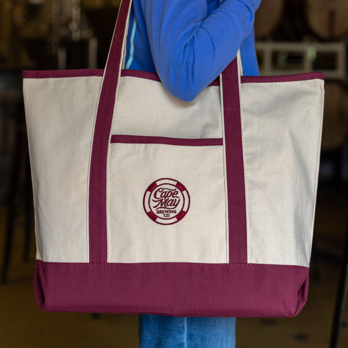 A person carrying a canvas tote with maroon trim and a round Cape May Brewing Co. logo