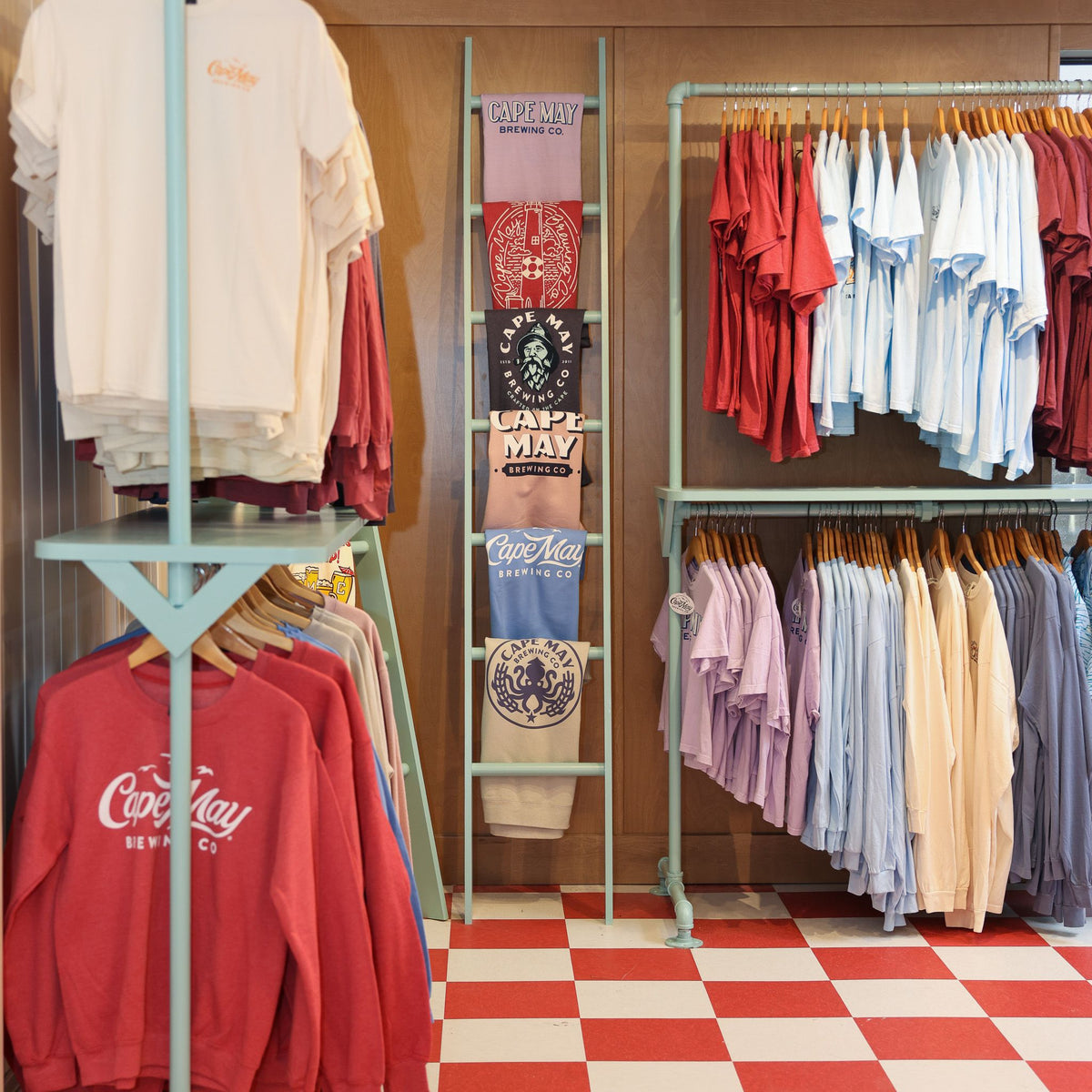 Racks and a display ladder of Cape May Brewing t-shirts and sweatshirts in the Brewtique on a red-and-white checkered floor